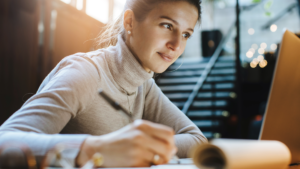 A women sitting by the table and writing something with a pen.